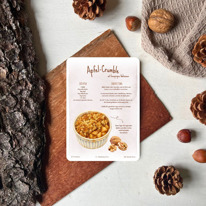Rezept für Apfelcrumble als Rezeptkarte abgebildet vor herbstlicher Deko von foodigence