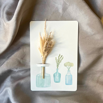 Postkarte von foodigence mit Sträußchen aus Wildgräsern in verschiedenen Vasen vor einem Satintuch