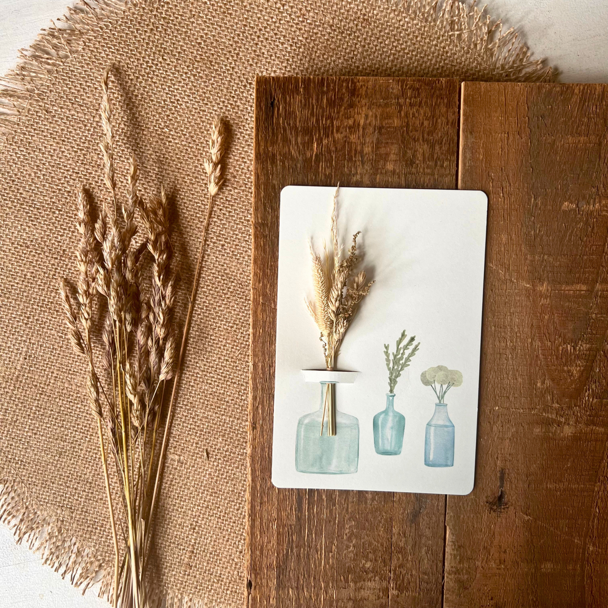 Postkarte von foodigence mit Sträußchen aus Wildgräsern in verschiedenen Vasen auf einer Holzplatte designt