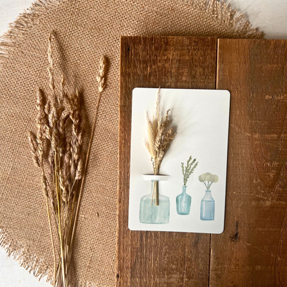Postkarte von foodigence mit Sträußchen aus Wildgräsern in verschiedenen Vasen auf einer Holzplatte designt