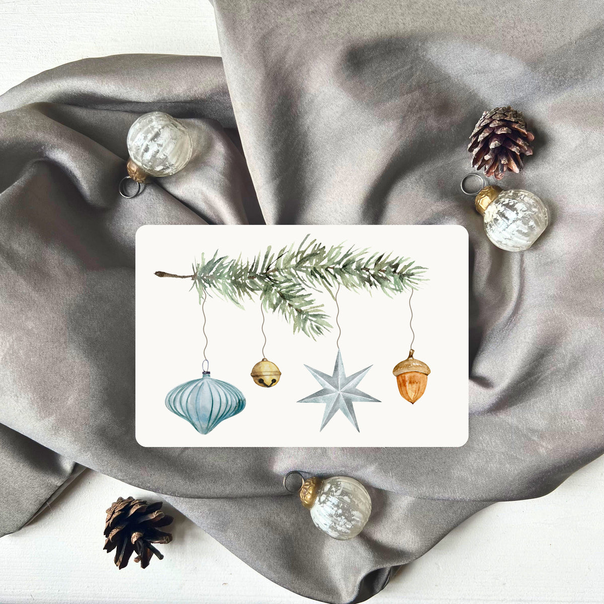 Weihnachtspostkarte von foodigence mit türkisen Weihnachtselementen in aquarell-Design vor einem grauen Samttuch abgebildet 