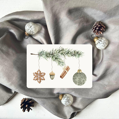 Weihnachtspostkarte von foodigence mit grünen Weihnachtselementen in aquarell-Design vor einem grauen Samttuch abgebildet 