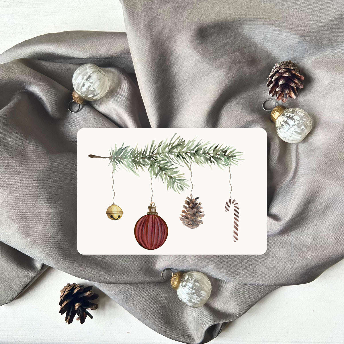 Weihnachtspostkarte von foodigence mit roten Weihnachtselementen in aquarell-Design vor einem grauen Samttuch abgebildet 