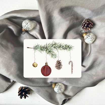 Weihnachtspostkarte von foodigence mit roten Weihnachtselementen in aquarell-Design vor einem grauen Samttuch abgebildet 