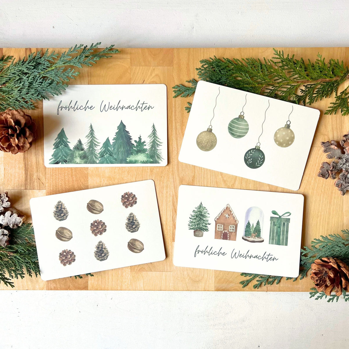 Postkarten als Set mit 4 weihnachtlichen Varianten in der Übersicht - Design mit Tannenbäumen, Weihnachtskugeln, Tannenzapfen & Nüssen und weihnachtlichen Motiven von foodigence