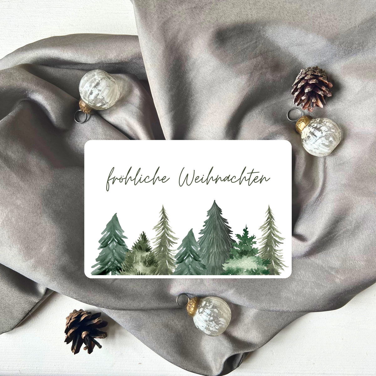 Karte mit grünen Tannenbäumen und Schriftzug "fröhliche Weihnachten" aus dem Weihnachtspostkarten Set von foodigence